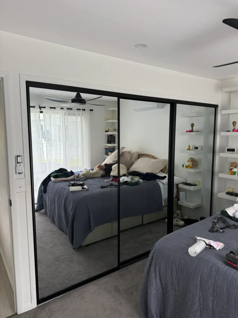 Three-panel mirror sliding wardrobe doors with black frame in a Brisbane bedroom